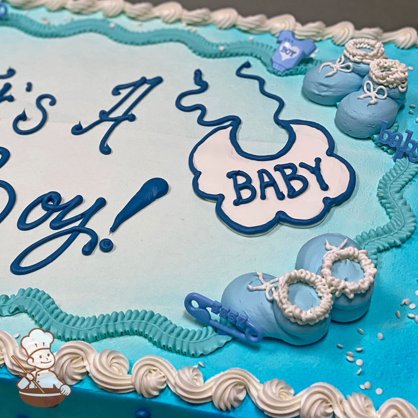 Light blue sheet cake with white buttercream borders, decorated with baby booties, a bib labeled "BABY," and plastic baby rings and safety pins.