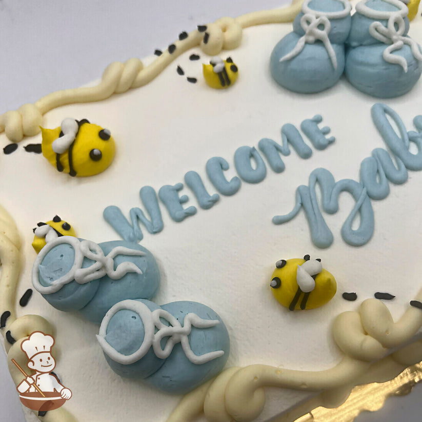 Sheet cake with pastel blue buttercream baby booties, yellow buttercream bees, and cream-colored piped borders. Bees have black stripes and white wings.