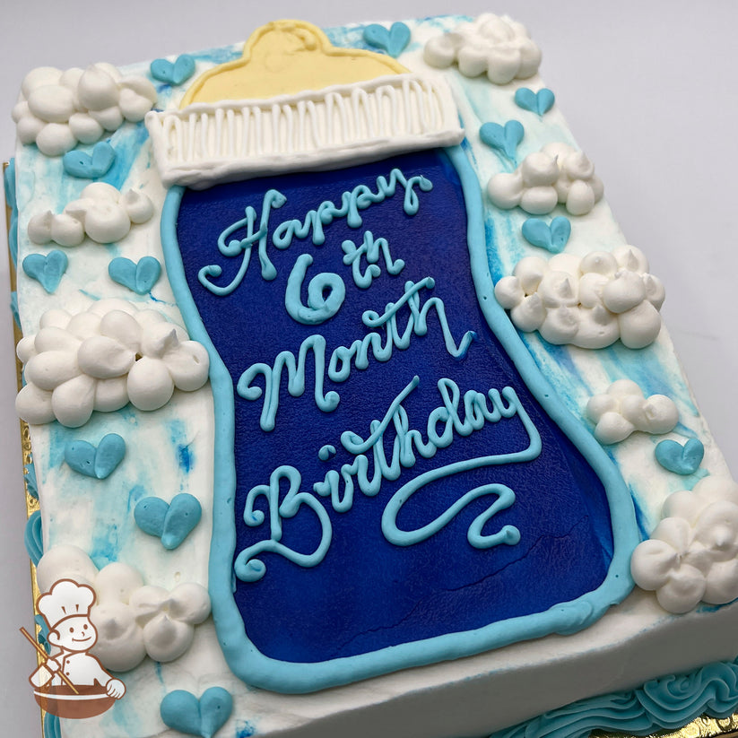 Sheet cake with a large blue baby bottle design, surrounded by buttercream clouds and light blue hearts on a white and blue marbled background.