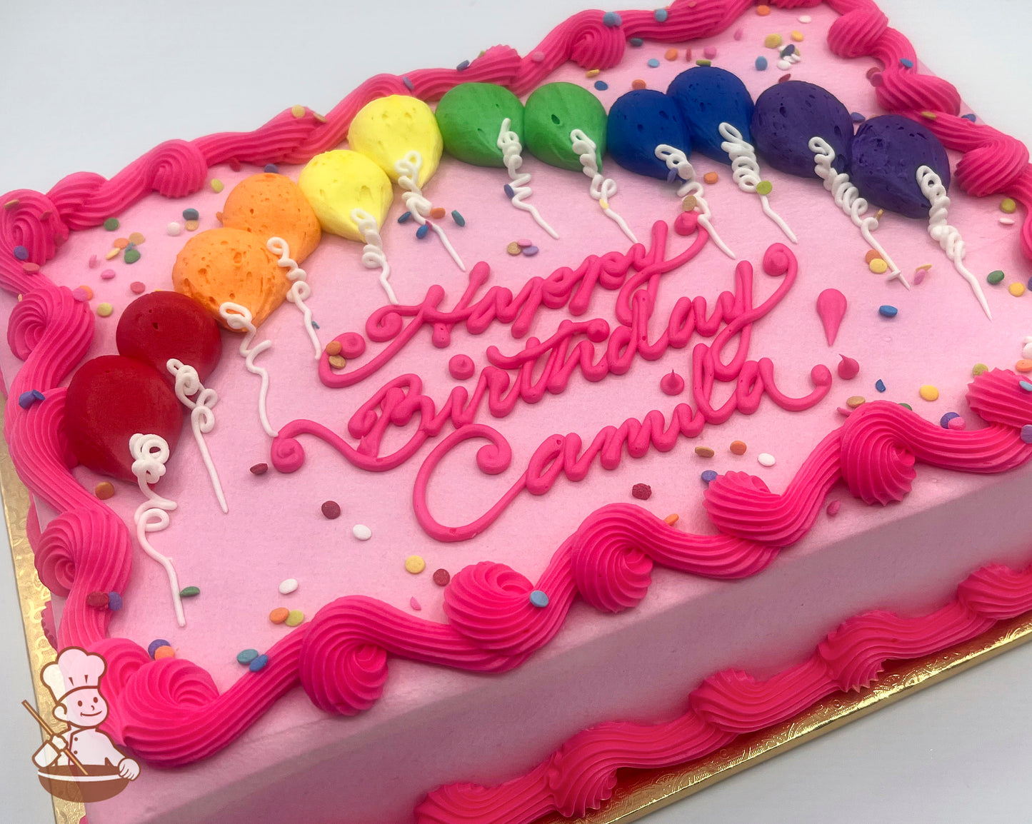 Pink sheet cake with colorful buttercream balloon decorations in a rainbow pattern, pink piped borders, and scattered sprinkles.