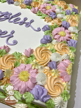 Sheet cake with buttercream decorations featuring a border of pastel florals, including pink blossoms, purple bell flowers, yellow star tips, and white rosettes.