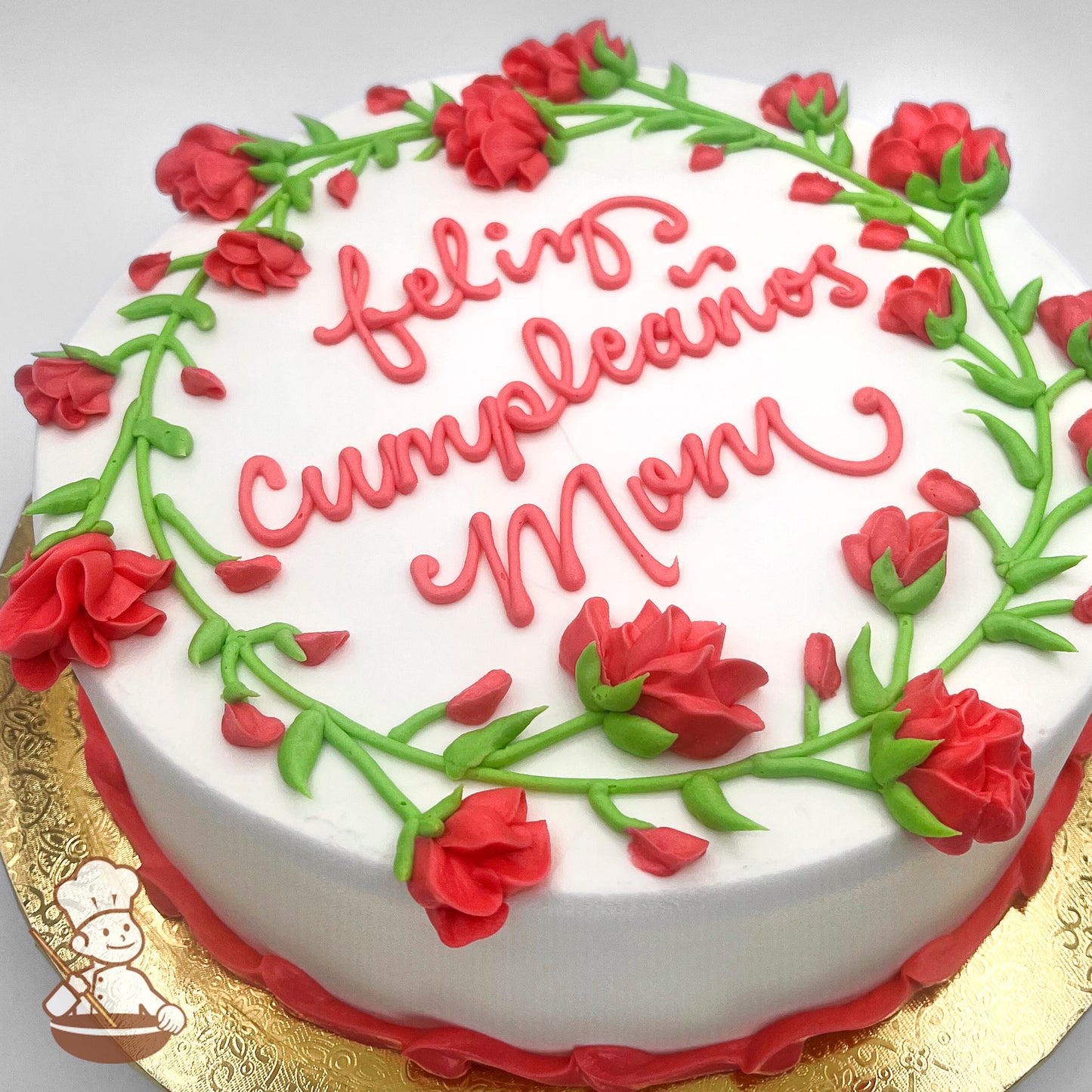 Round white cake decorated with vibrant pink buttercream bell flowers and green vines forming a wreath around the top edge.