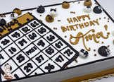 Sheet cake with buttercream bingo card and balls, decorated in black, white, and gold. Gold, black and white buttercream dots scattered around.