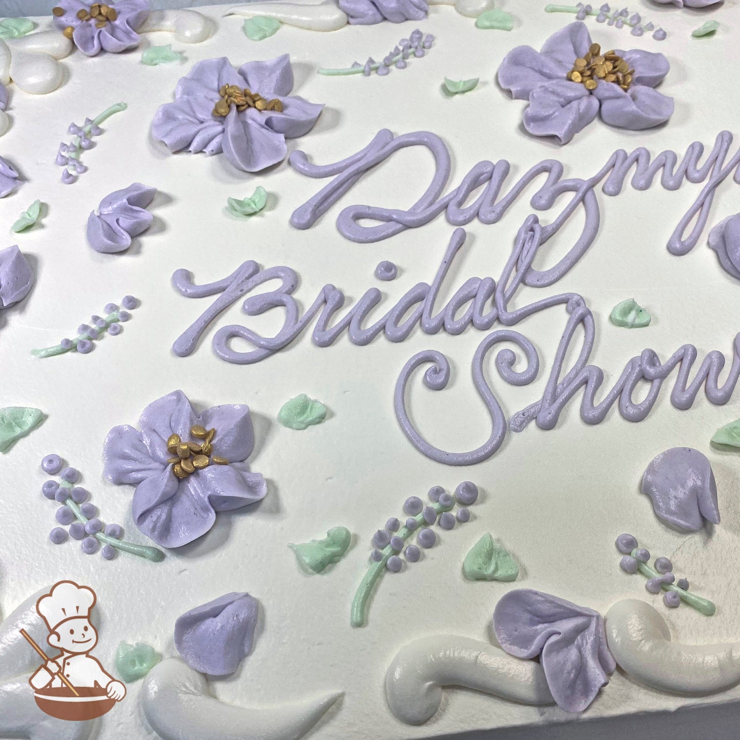 Sheet cake with lavender buttercream flowers, green leaves, and small floral accents. Decorated with piped swirls and delicate blossoms.
