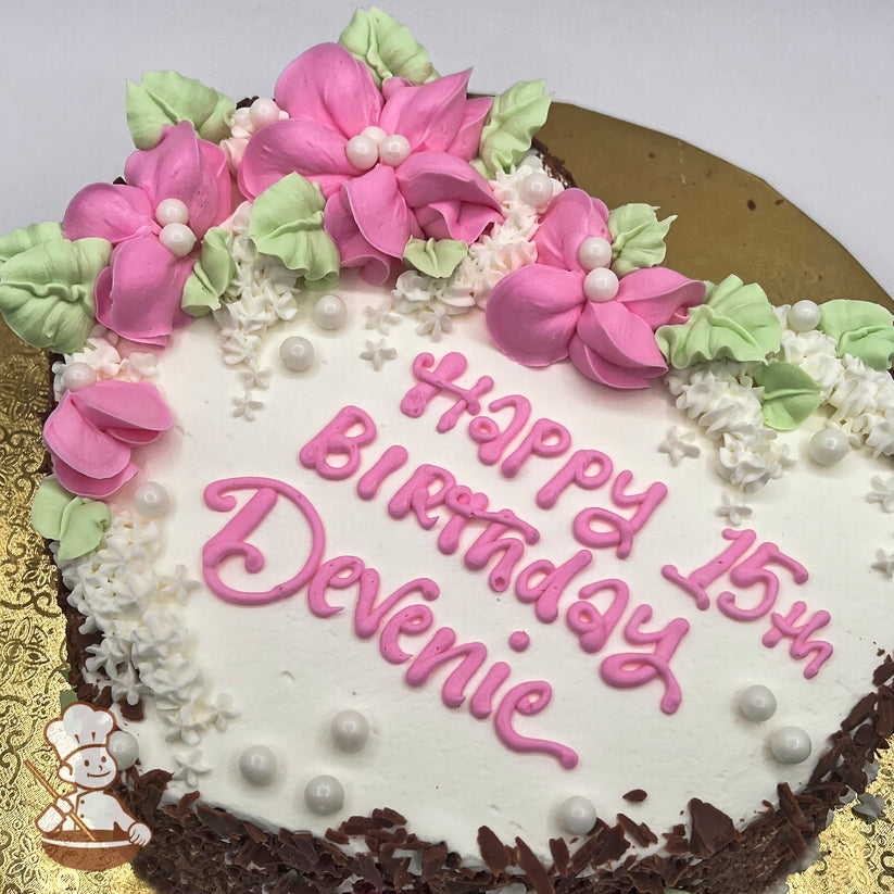 Round cake with pink buttercream blossoms, green leaves, white sugar pearls, and small white flowers on a white frosting base.