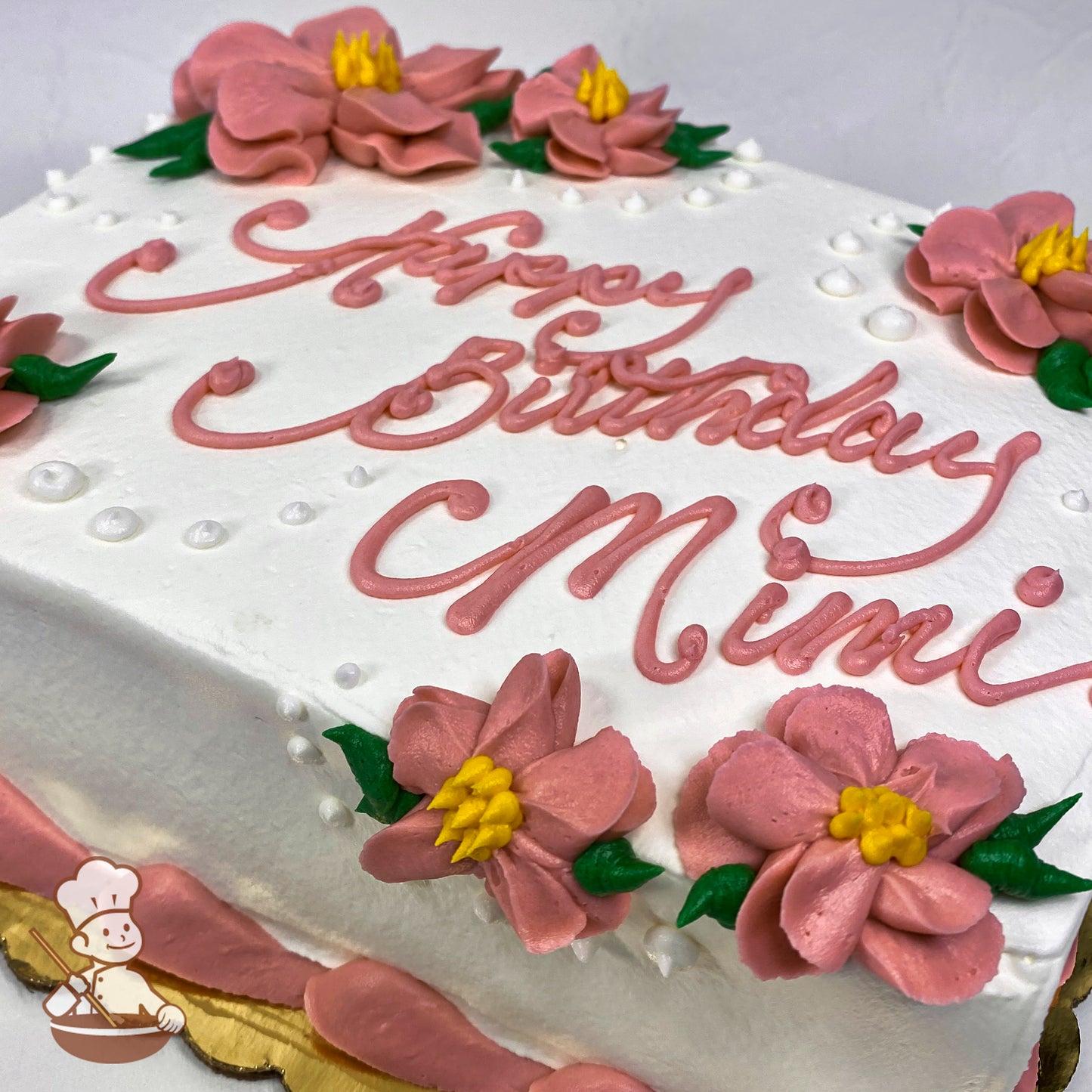 White sheet cake with pink buttercream flowers, yellow centers, green leaves, and small white dot accents. Pink border along the base.