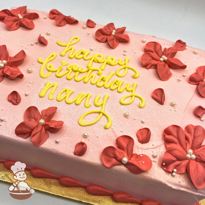 Pink sheet cake with light red buttercream blossoms adorned with white sugar pearls, and scattered petals on a gold base.