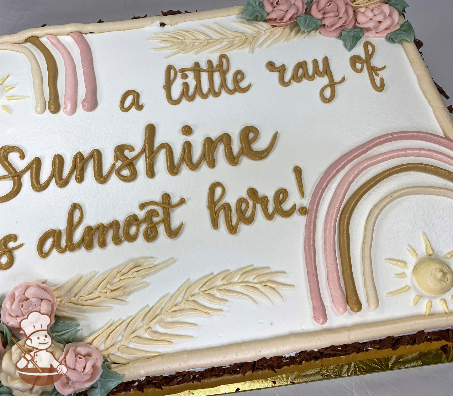 Sheet cake with white frosting, decorated with pastel boho rainbow, golden sun, beige leaves, and pink buttercream roses with green leaves.