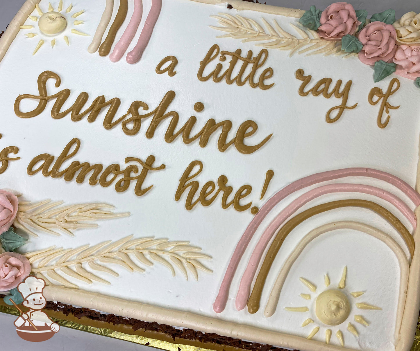 Sheet cake with white frosting, decorated with pastel boho rainbow, golden sun, beige leaves, and pink buttercream roses with green leaves.
