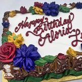 Sheet cake with buttercream decorations featuring a branch border with assorted florals: red roses, blue flowers, yellow flowers, and green leaves.