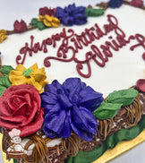 Sheet cake with buttercream decorations featuring a branch border with assorted florals: red roses, blue flowers, yellow flowers, and green leaves.