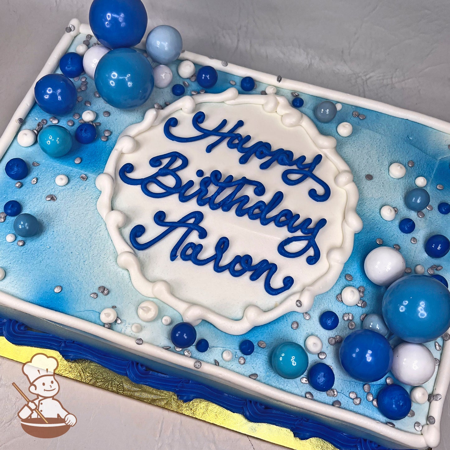 Sheet cake with blue and white buttercream decorations, featuring bubble toppers in various sizes and shades of blue and white, with silver sprinkles.