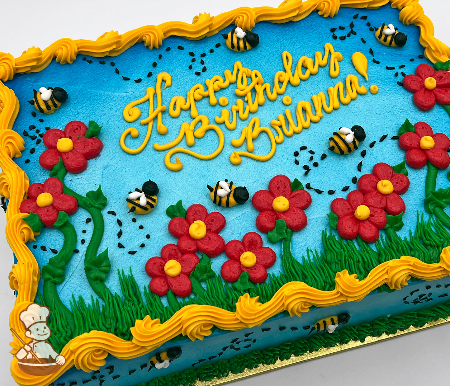 Sheet cake with blue base, red daisies with yellow centers, green leaves and grass, buzzing bees with black dotted flight paths, and yellow border frosting.
