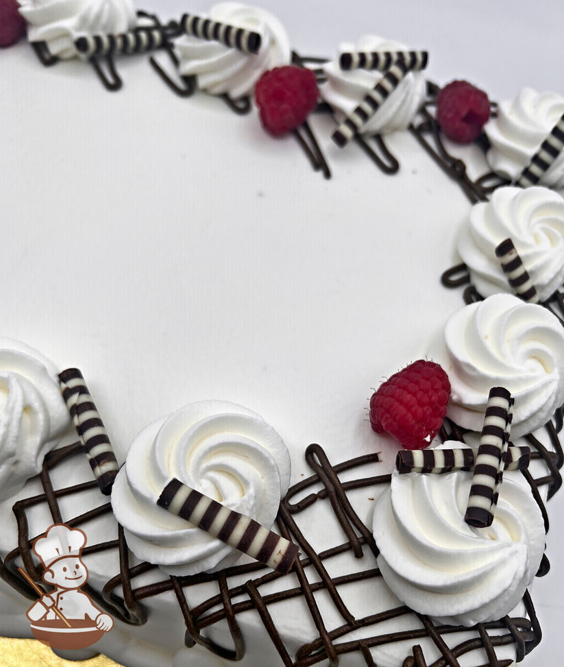 White sheet cake with buttercream swirls, striped chocolate stix, chocolate drizzle accents, and fresh raspberries arranged on top.