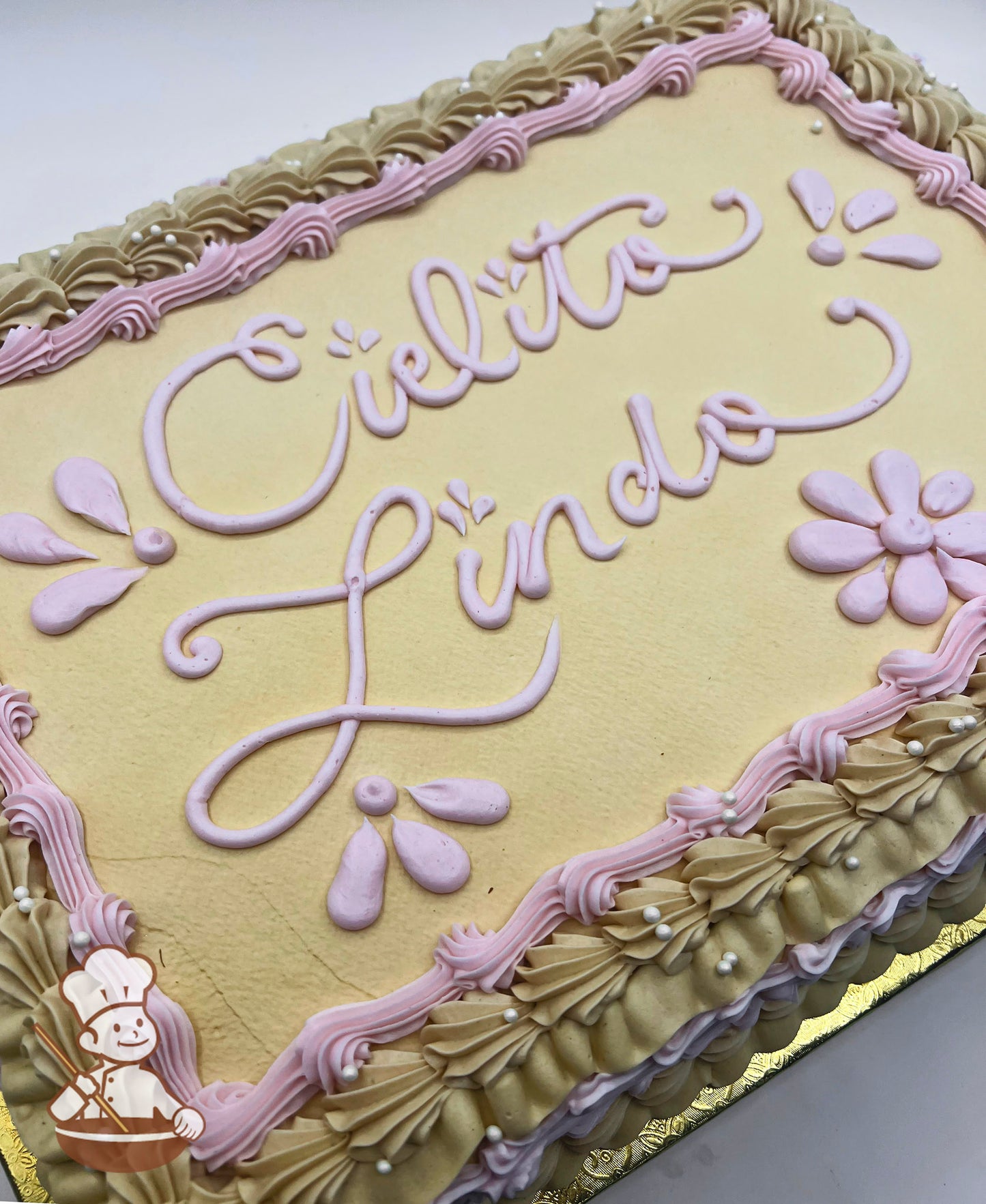 Sheet cake with beige frosting, pink piped floral designs, and a decorative border of beige and pink swirls accented with white pearls.