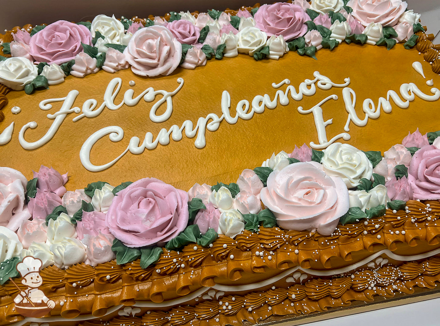 Sheet cake with golden frosting, decorated with pink and white buttercream roses, green leaves, and piped borders with white pearl accents.