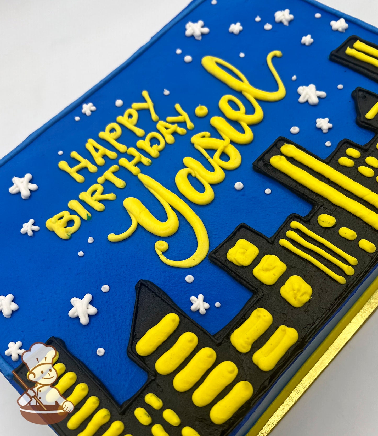 Sheet cake with blue base, black and yellow buttercream city skyline design, white buttercream stars and dots resembling a night sky.