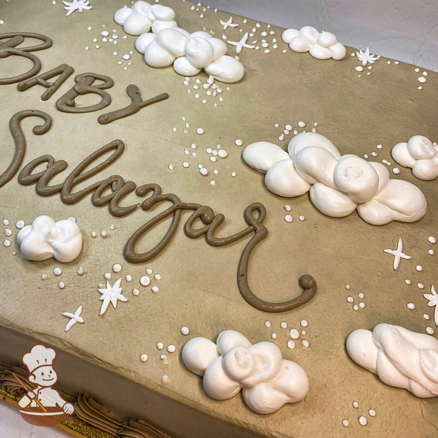 Sheet cake with beige base, decorated with white buttercream clouds, small white sparkles, and star-shaped accents.