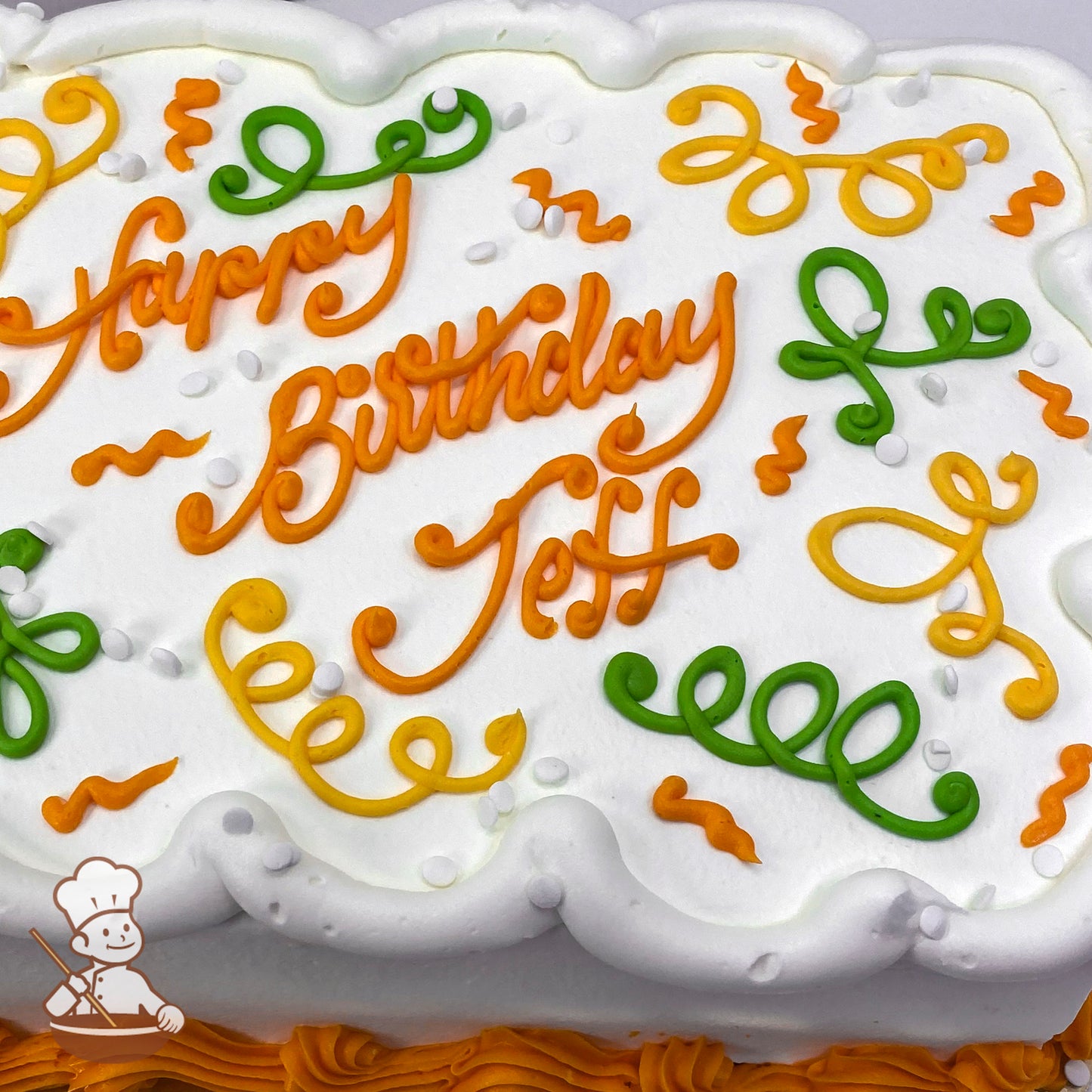Sheet cake with white frosting, decorated with orange, yellow, and green ribbon scrolls, white confetti sprinkles, and orange border piping.