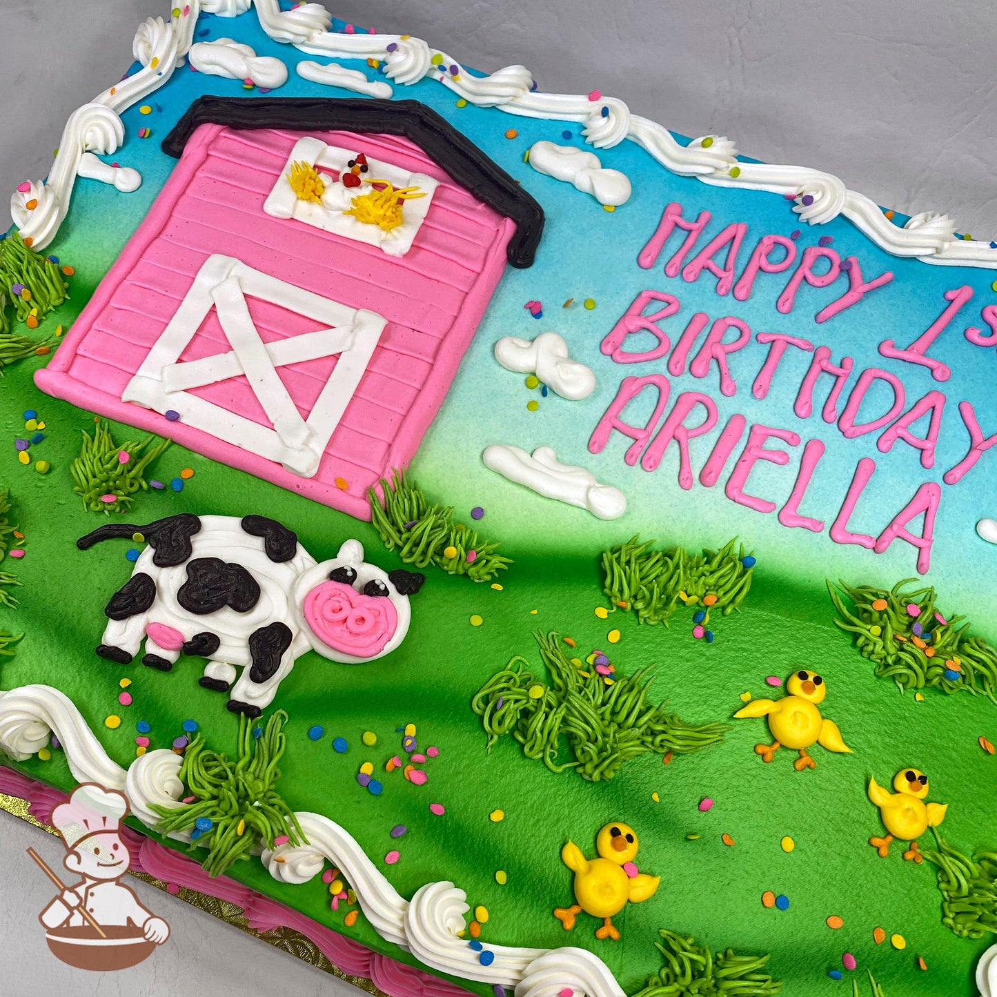 Sheet cake with buttercream decorations featuring a pink barn, black-and-white cow, yellow chicks, green grass, white clouds, and colorful sprinkles.