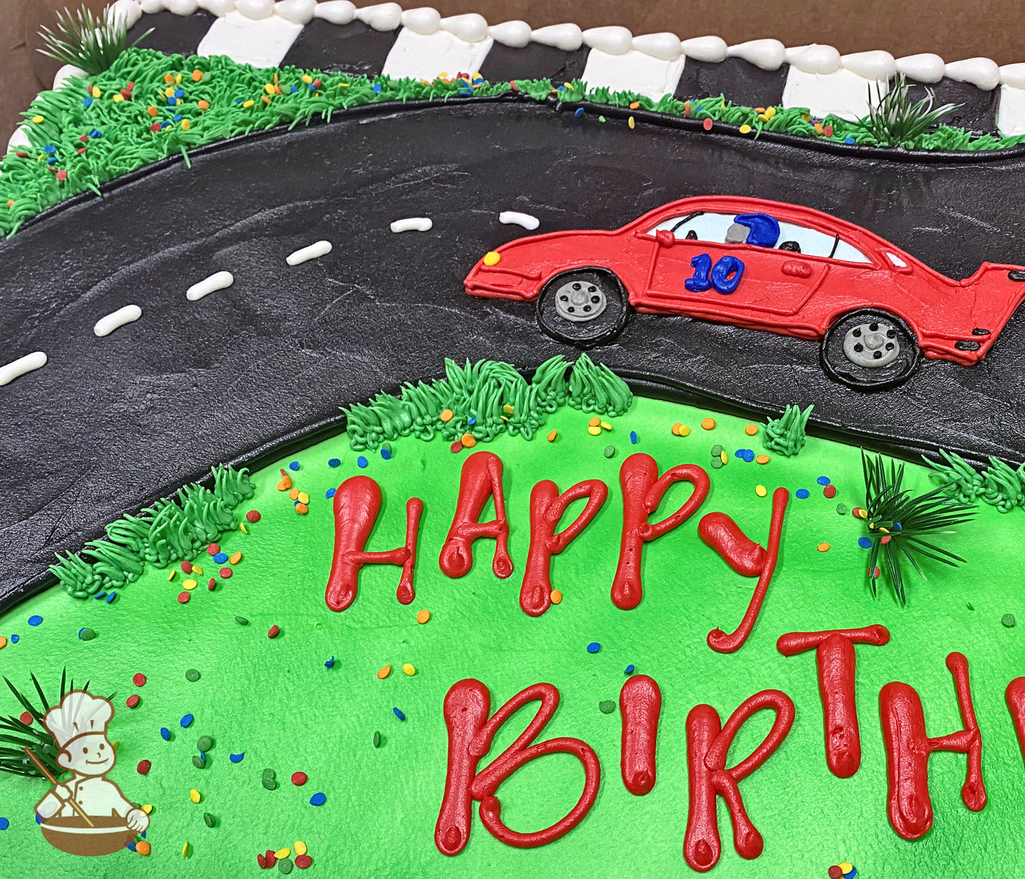 Sheet cake with a buttercream race track, red race car, and green grass. Colorful sprinkles and plastic palm trees decorate the cake.