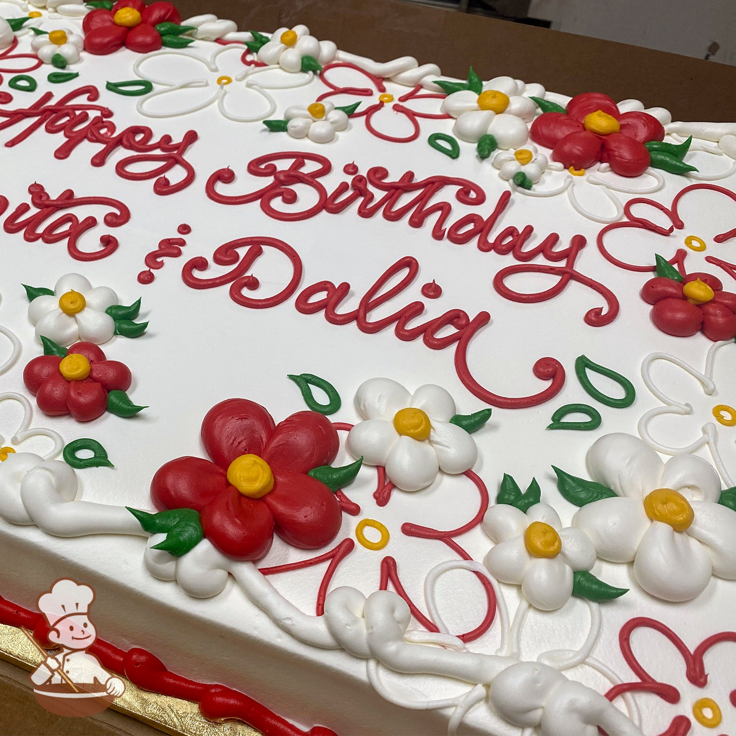 Sheet cake with white frosting, decorated with red and white daisy flowers, yellow centers, green leaves, daisy scrolls, and a red border.