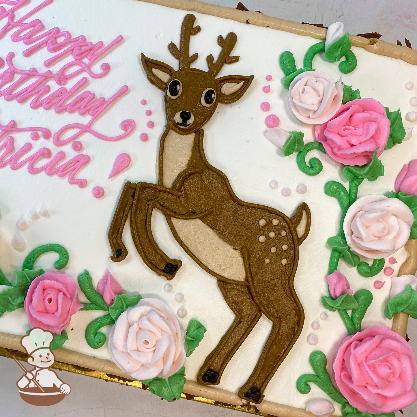 Sheet cake with a hand-piped deer and pink roses in buttercream. The deer is detailed with antlers and spots, surrounded by green leaves.