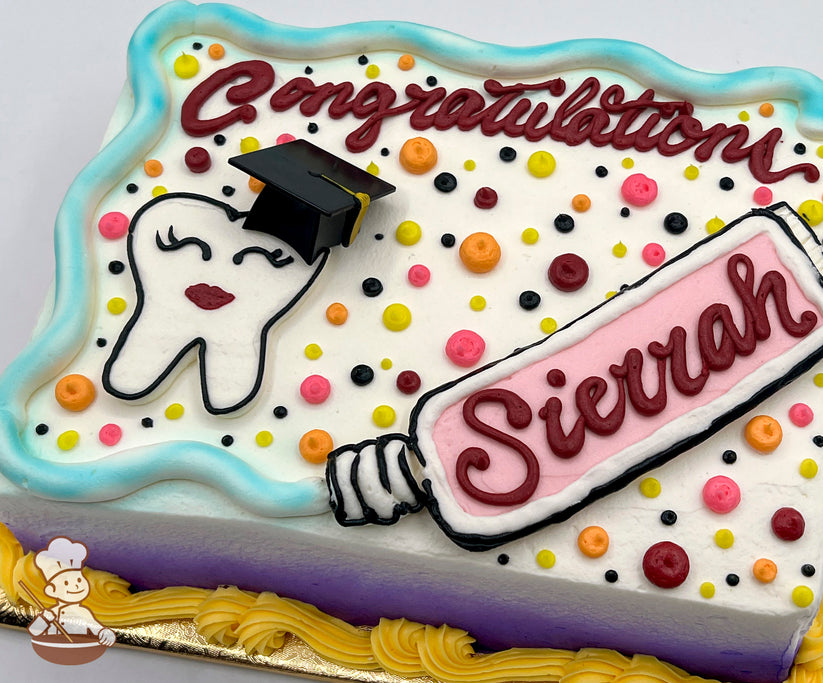 Sheet cake with buttercream decorations, featuring a hand-piped smiling tooth wearing a graduation cap, a pink toothpaste tube, colorful dots, and a blue border.