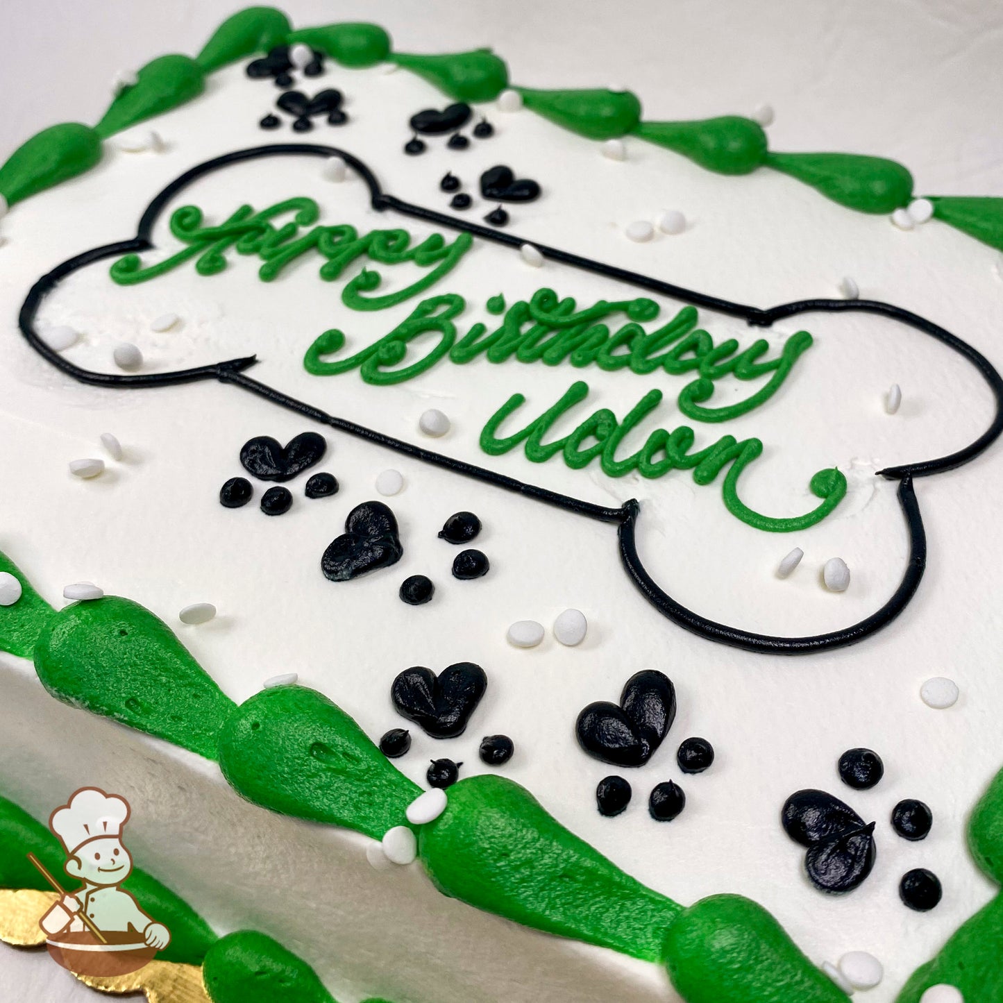 Sheet cake with white icing, green piped border, black paw prints, white sprinkles, and a large black-outlined dog bone decoration.