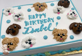 Sheet cake with buttercream dog faces, including brown and white dogs, and blue dots. Blue and green piping decorates the borders.
