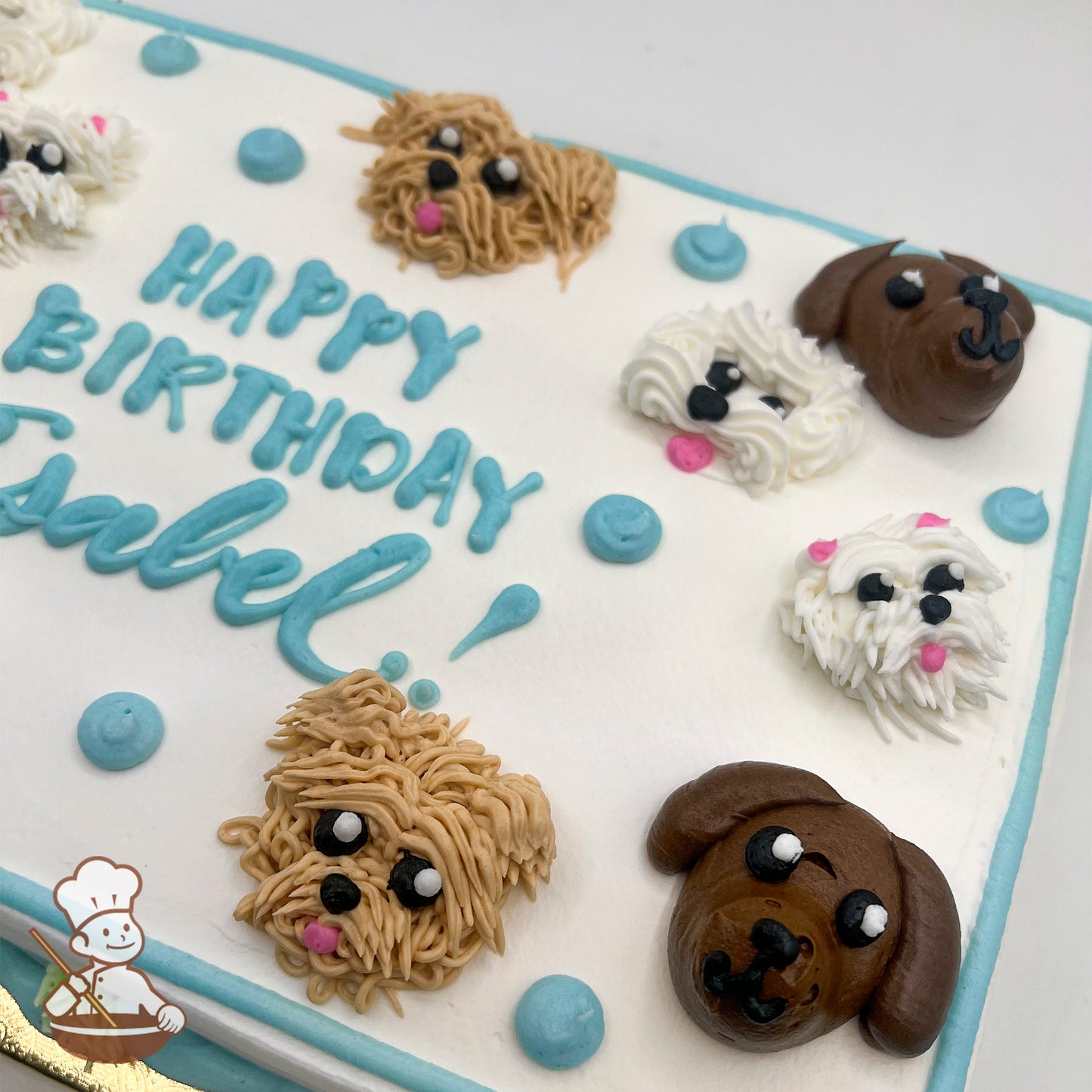 Sheet cake with buttercream dog faces, including brown and white dogs, and blue dots. Blue and green piping decorates the borders.