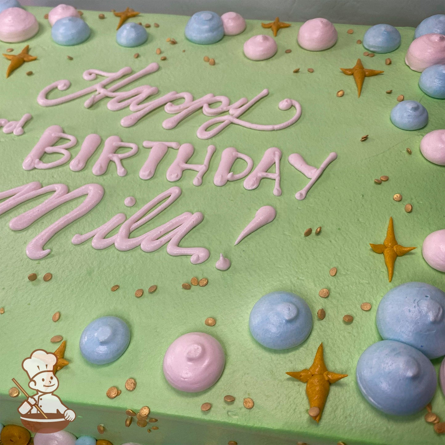 Light green sheet cake with pink and blue buttercream dollops, gold star-shaped sparkles, and small gold sprinkles scattered on top.