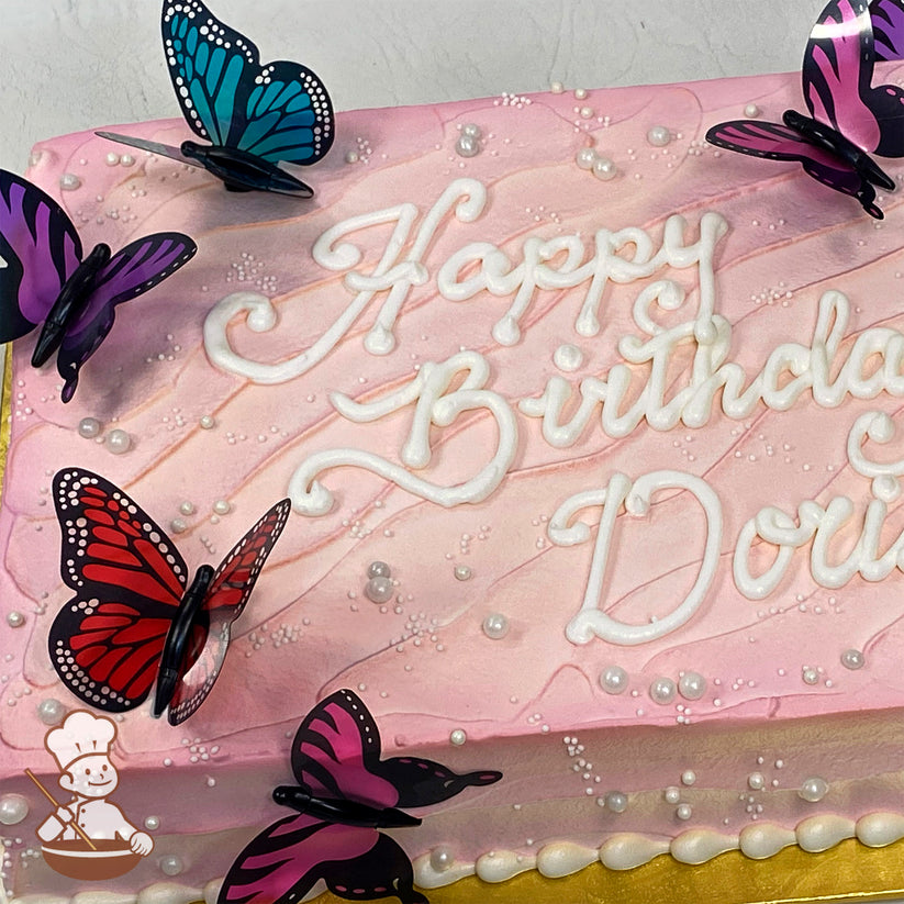 Pink sheet cake with icing texture, adorned with plastic butterflies in red, purple, and blue, and scattered pearls.