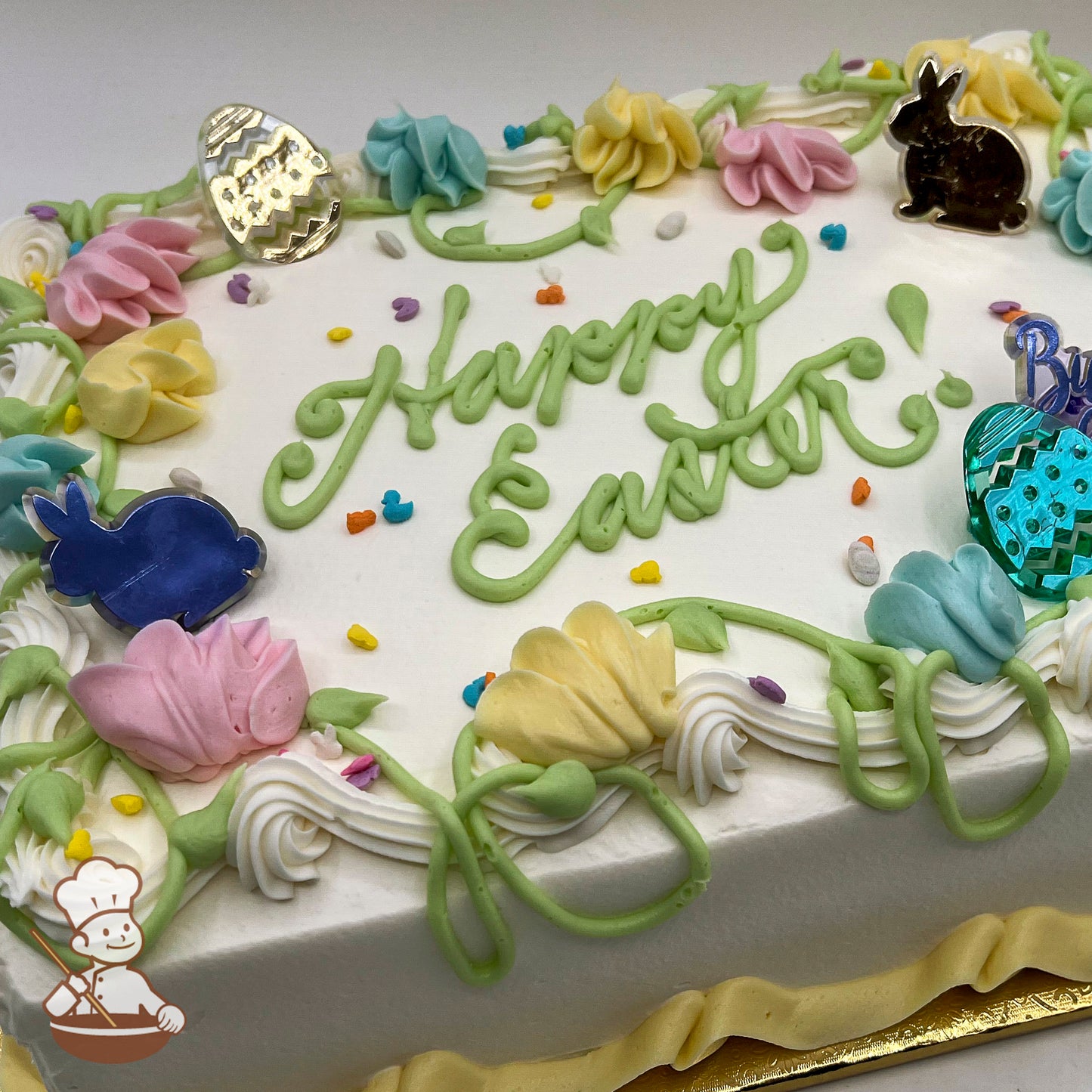 Sheet cake with buttercream flowers, vines, and plastic Easter toppers shaped like bunnies and eggs. Pastel colors and festive decorations.