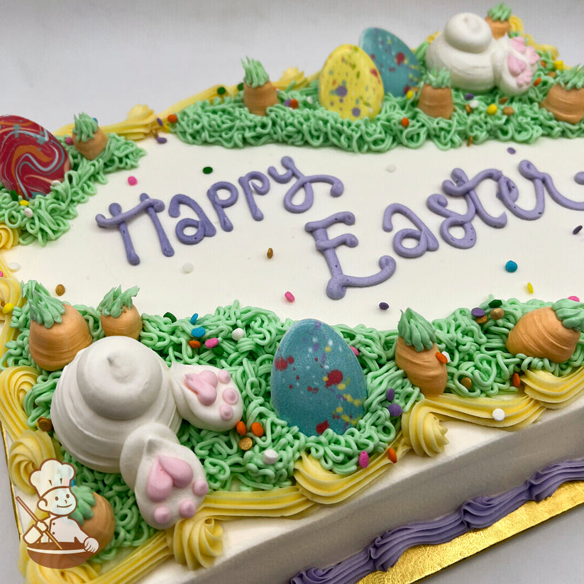 Sheet cake with white frosting, green grass piping, plastic Easter egg toppers, buttercream carrots, and a bunny tail with pink paw prints.