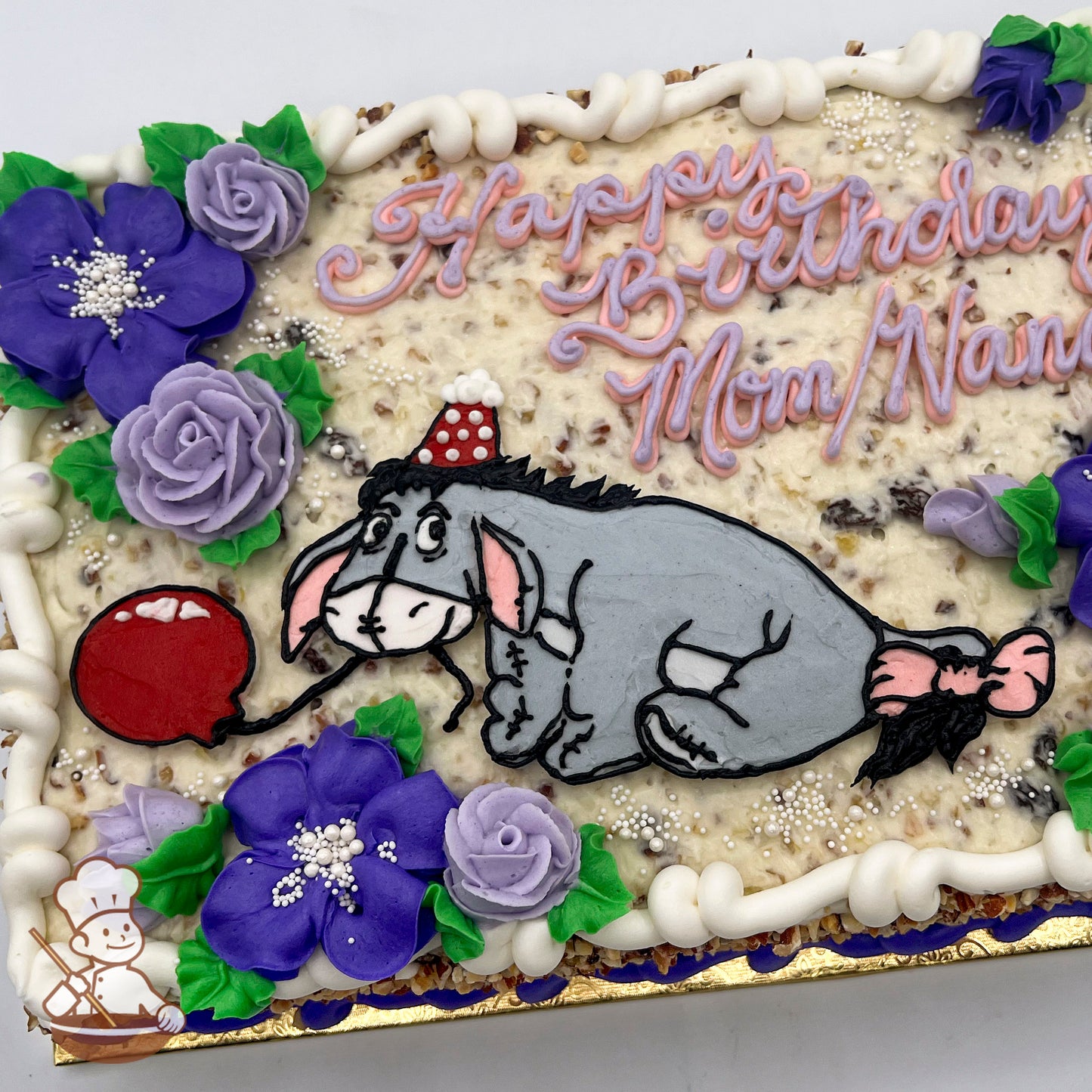 Sheet cake with a hand-piped Eeyore holding a red balloon, surrounded by purple and lavender buttercream flowers with green leaves and white pearl accents.