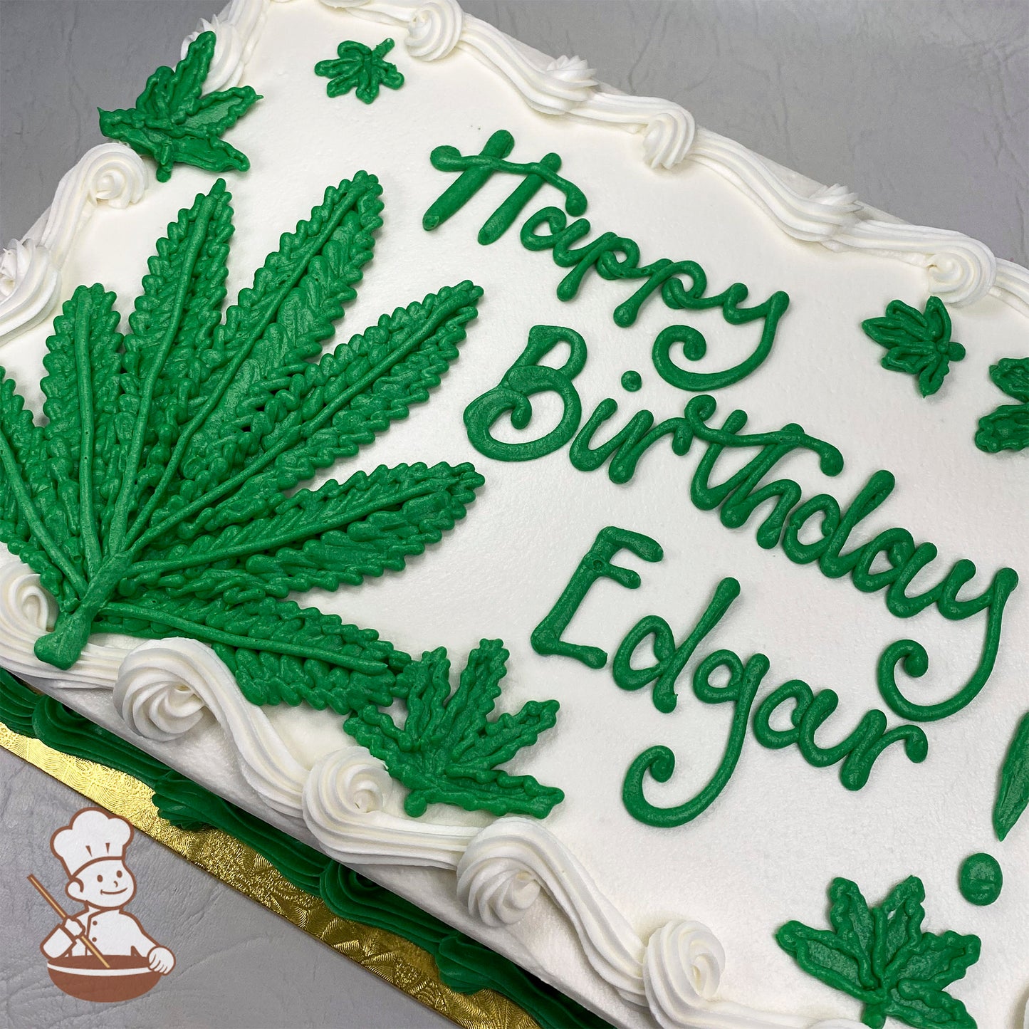 White sheet cake with green buttercream marijuana leaves and white swirls on the border.