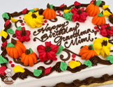 Sheet cake with buttercream decorations of orange pumpkins, red and yellow blossoms, and green leaves, bordered by brown swirls.