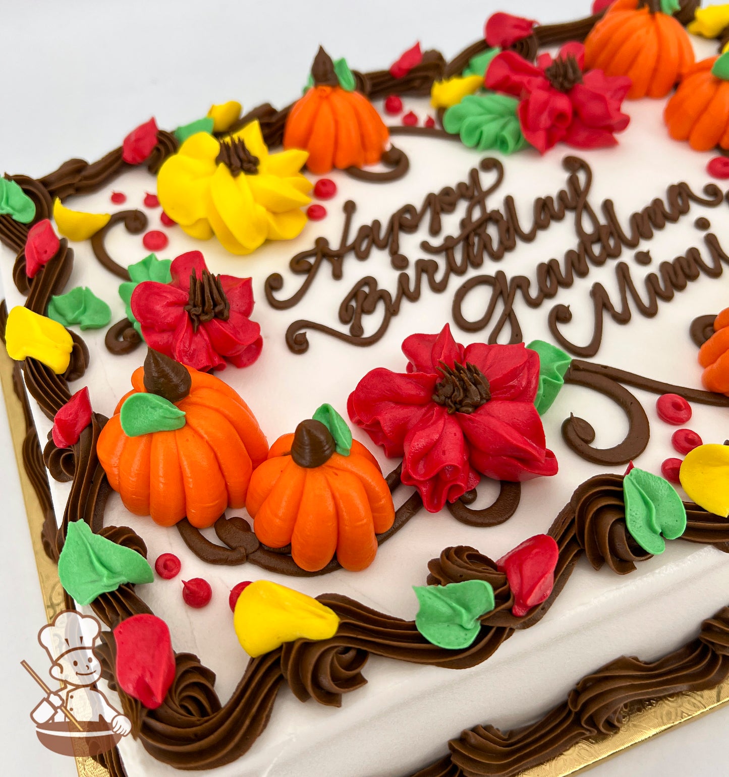 Sheet cake with buttercream decorations of orange pumpkins, red and yellow blossoms, and green leaves, bordered by brown swirls.