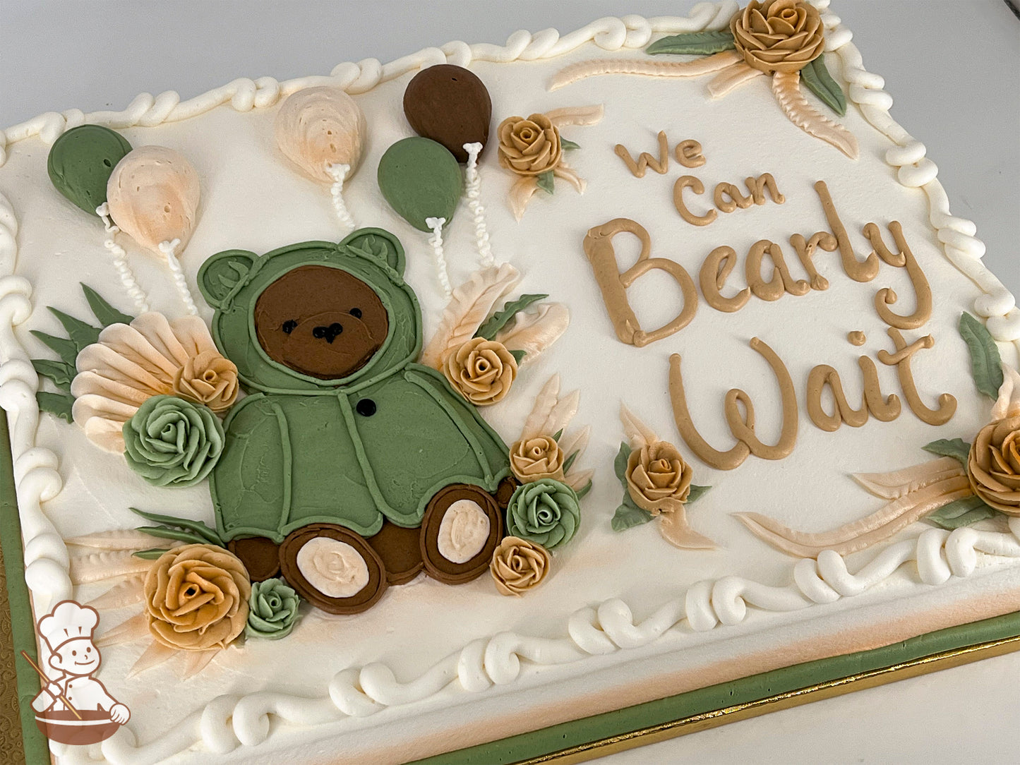 Sheet cake with buttercream decorations, featuring a hand-piped bear in a green sweater, surrounded by roses, balloons, and leafy accents.