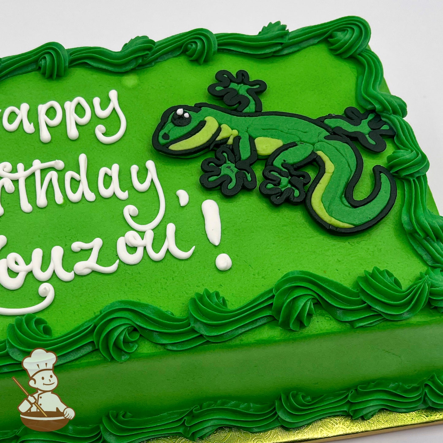 Green sheet cake with piped green buttercream borders and a decorative gecko design made of icing in shades of green and black.