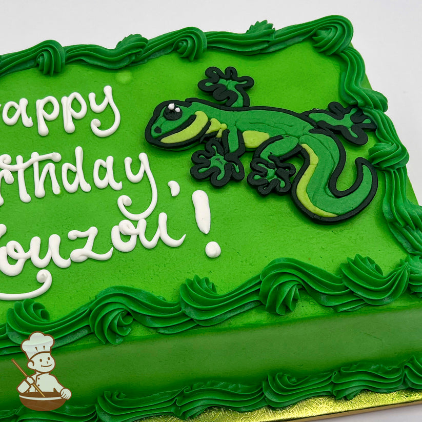 Green sheet cake with piped green buttercream borders and a decorative gecko design made of icing in shades of green and black.