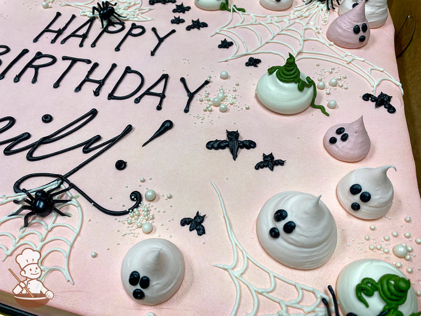 Pink sheet cake with buttercream ghosts, black bats, white spider webs, plastic spiders, and scattered white sugar pearls for decoration.