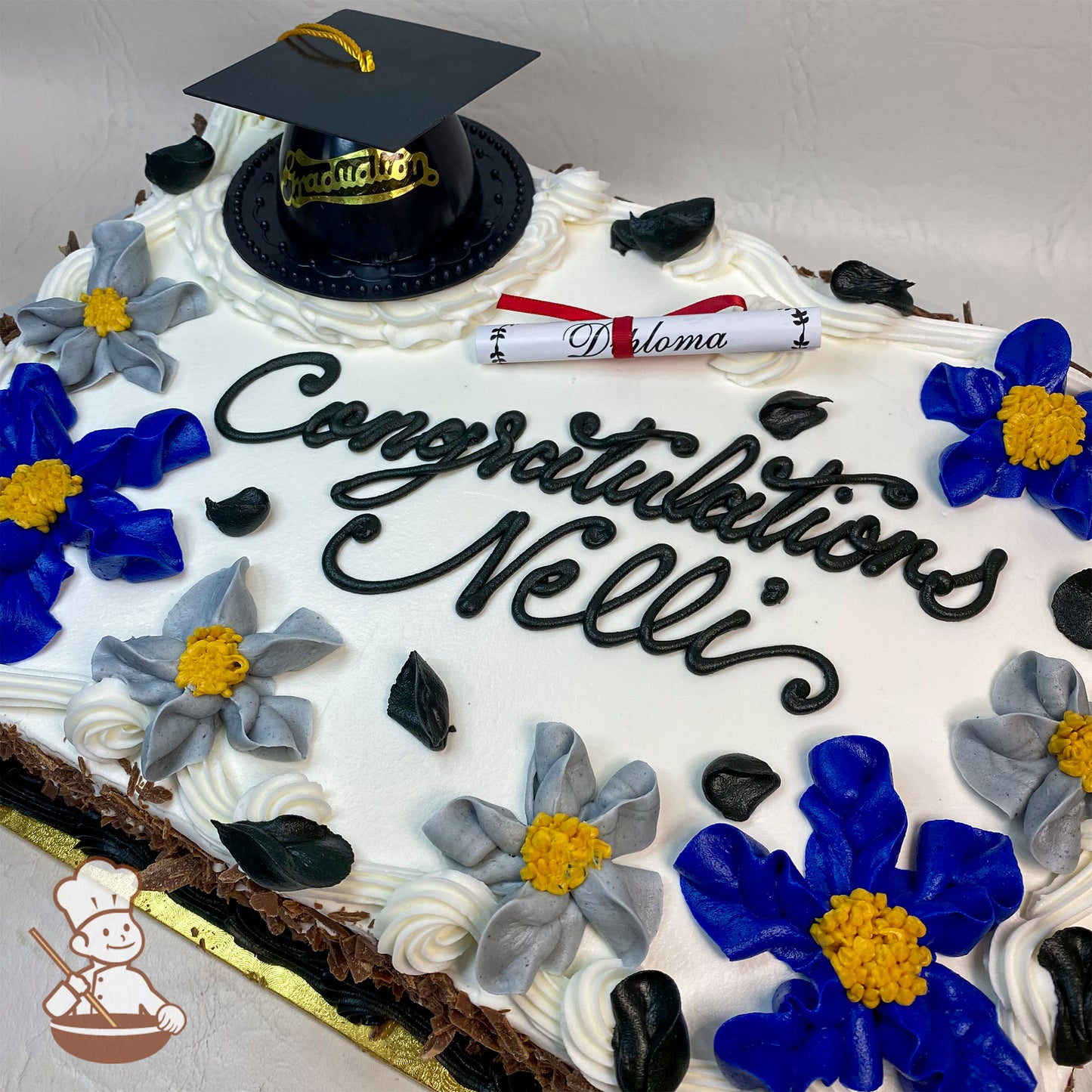 Sheet cake with white frosting, decorated with blue and gray Hawaiian flowers, a plastic black graduation cap, and a paper diploma.