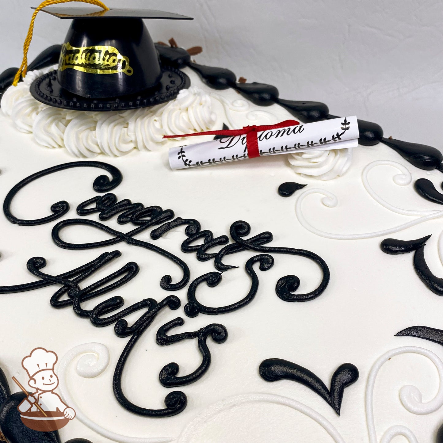 Sheet cake with white frosting, black decorative swirls, a plastic black graduation cap with a gold tassel, and a rolled paper diploma tied with a red ribbon.
