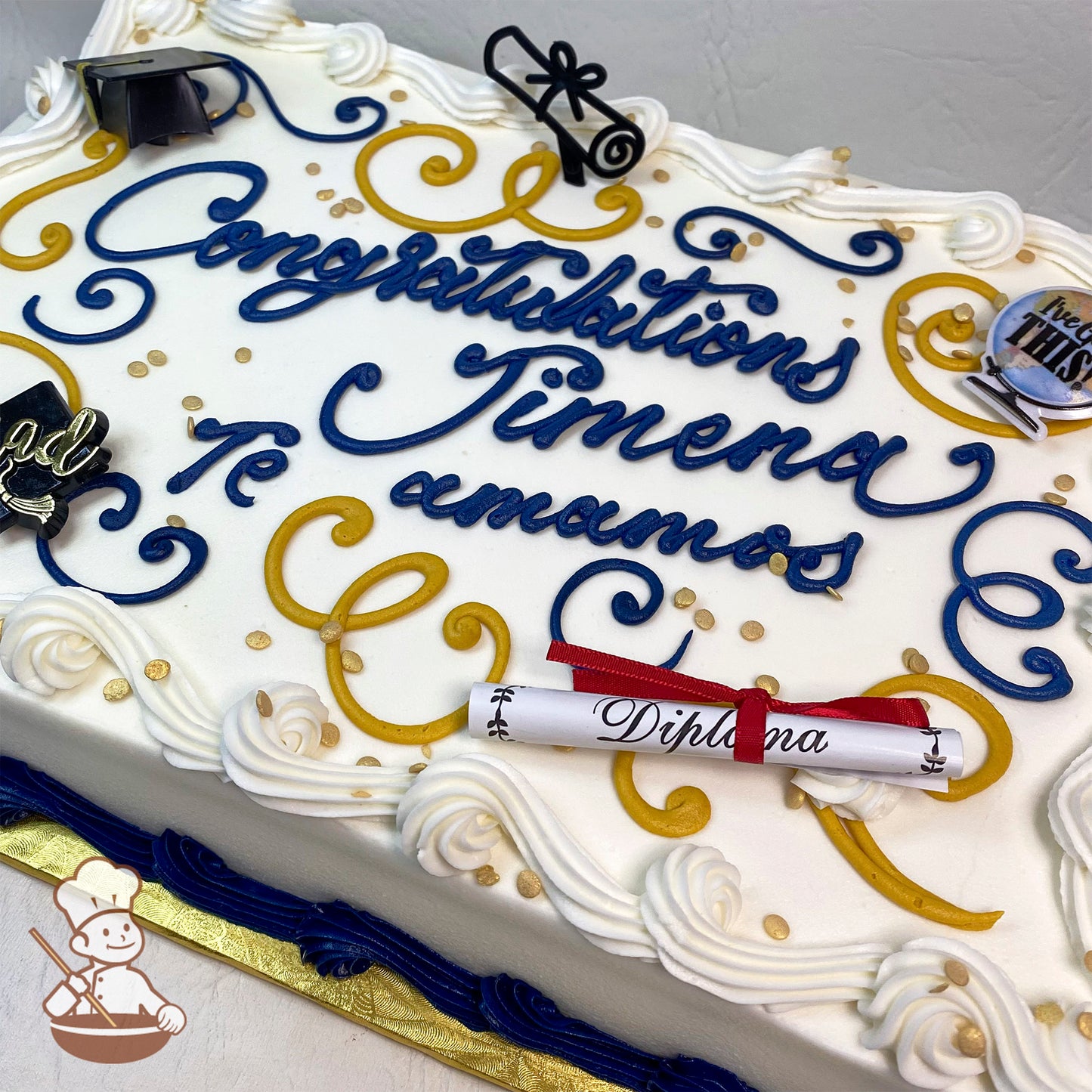 Sheet cake with gold and blue buttercream scrolls, plastic grad cap, diploma, and confetti.