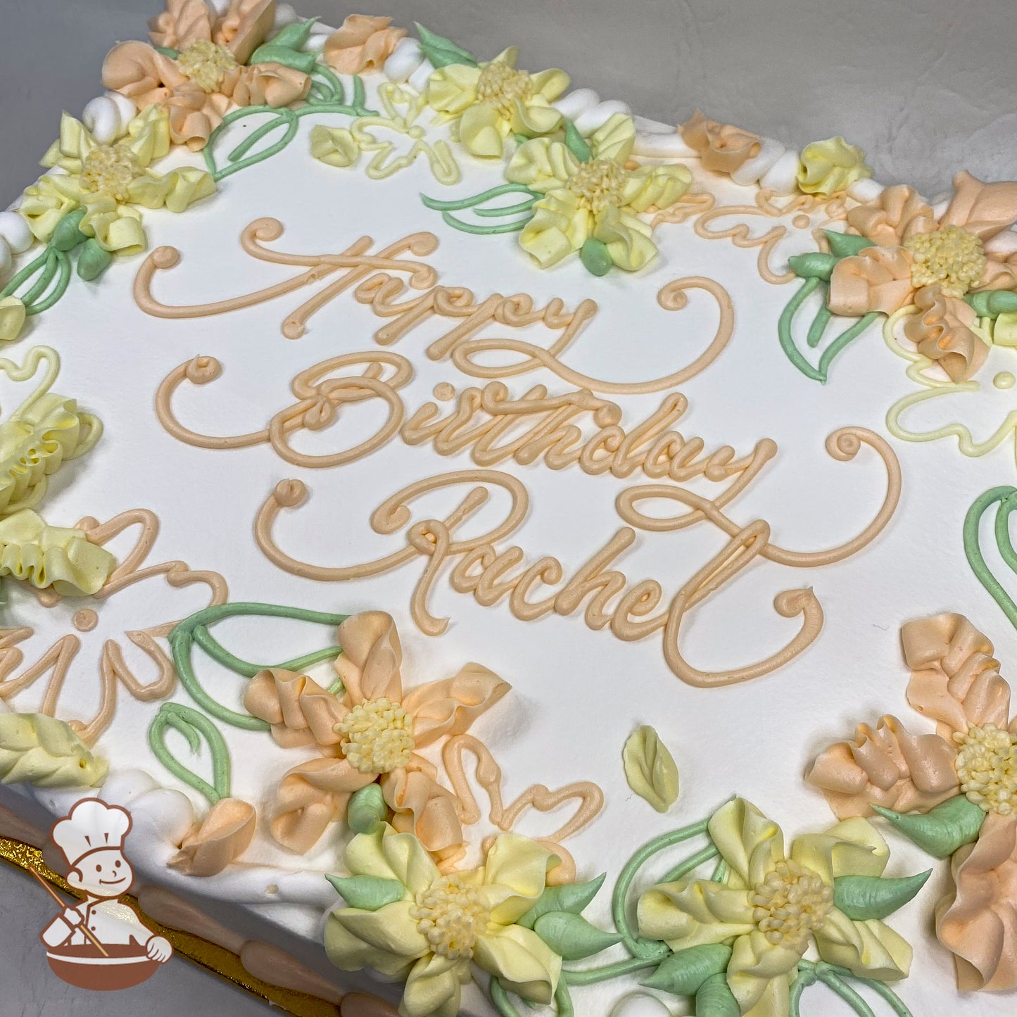 Sheet cake with buttercream decorations, featuring Hawaiian flowers in pastel yellow and peach, with green leaves and floral scrolls.