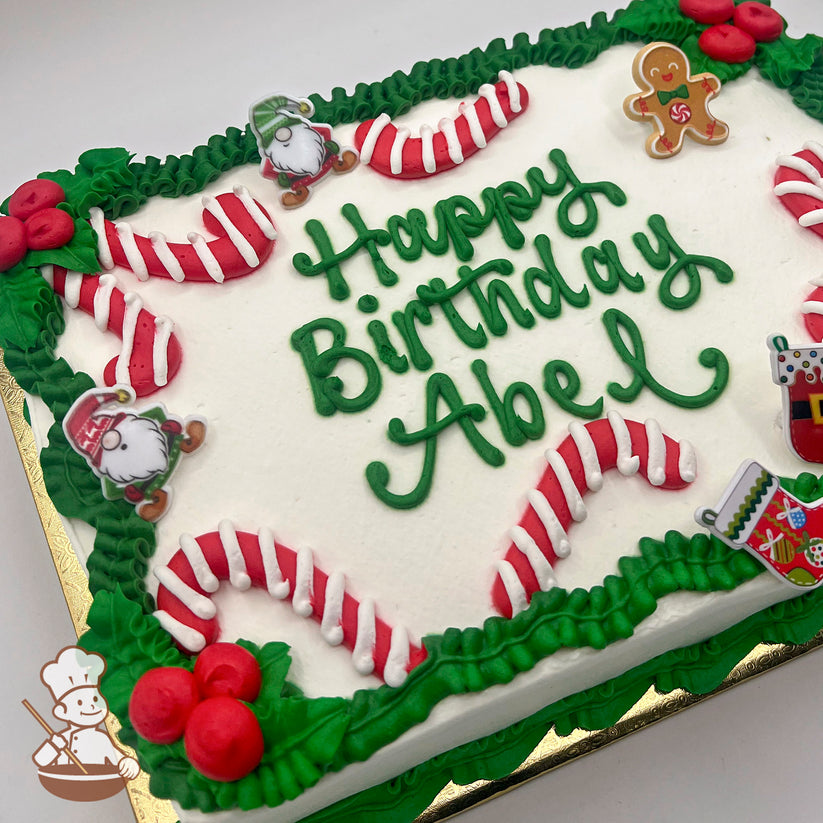 Sheet cake with buttercream candy canes, green leaves, red berries, plastic gnomes, gingerbread man, and Christmas stocking decorations.