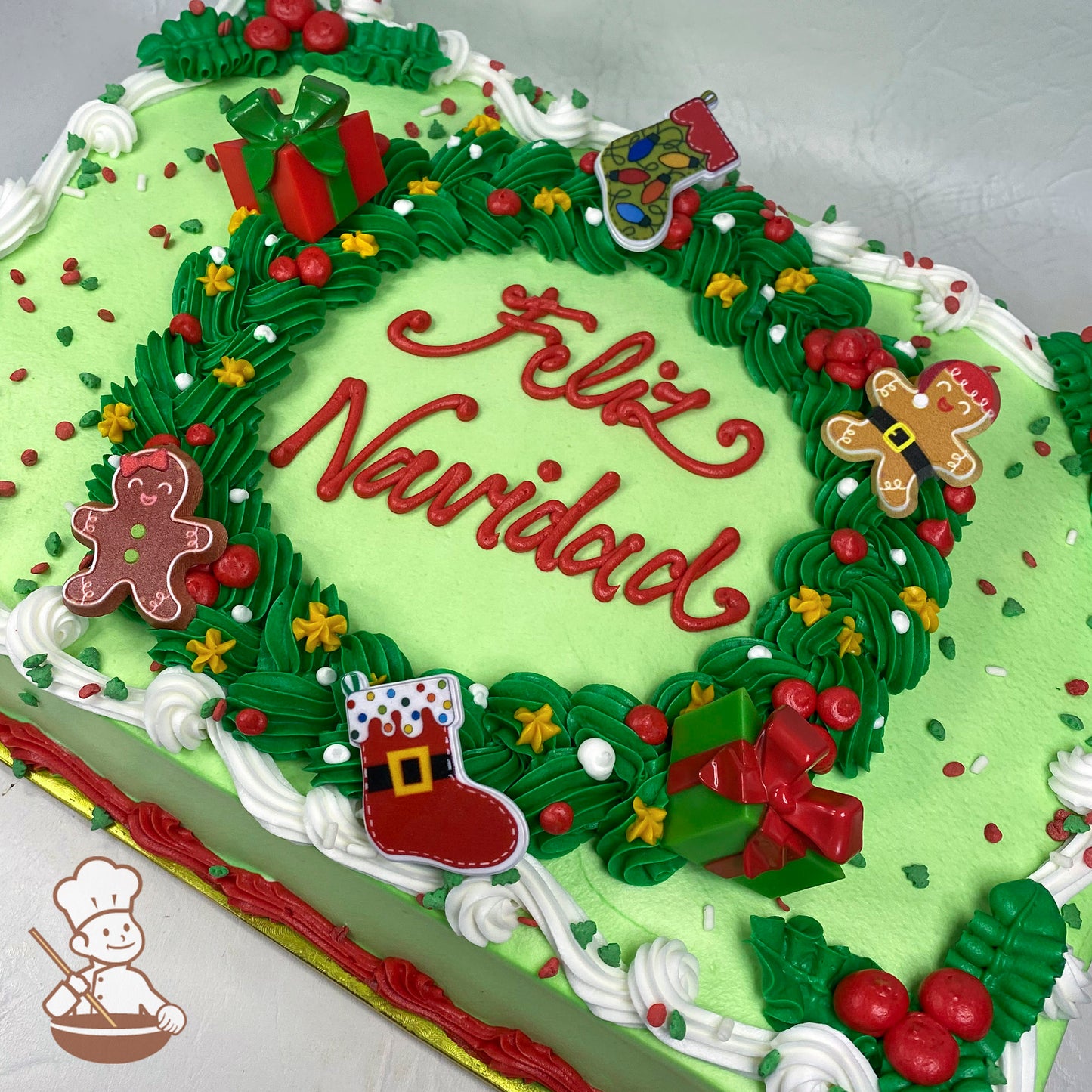Green sheet cake with a piped buttercream holiday wreath, decorated with red berries, yellow stars, gingerbread figures, stockings, and gift-shaped plastic toppers.