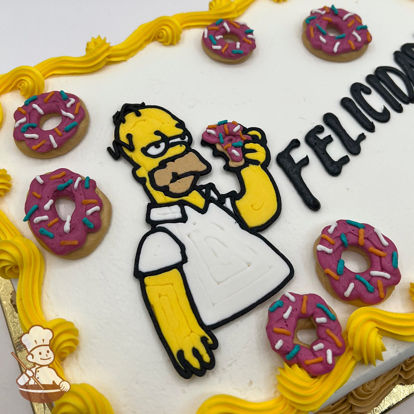Homer Simpson made of icing holds a pink sprinkled donut on a white sheet cake, decorated with yellow buttercream trims and pink sprinkled donut designs.